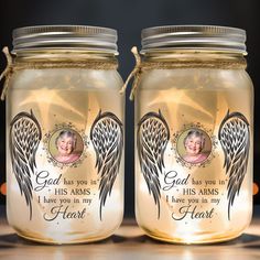 two mason jars with angel wings on them, one has an image of a woman's face and the other says god has in his arms i have you in my heart