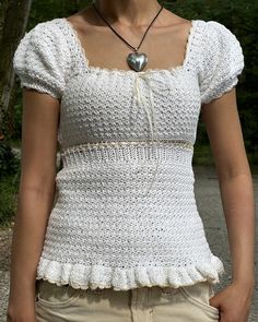 a woman wearing a white crochet top with a heart pendant on her necklace