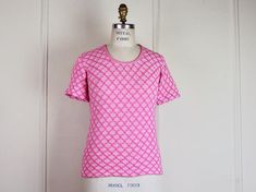 super fun shirt from the 1970s. hot pink argyle patterned double knit.  scoop neck.  short sleeves.  tight and fitted and super cute!!!tagged ♥ 75% orlon, 25% antronmachine wash and drymeasurements ♥ best fits: small to mediumshoulder seam to shoulder seam: 13.5 inchesbust: 15.5 incheswaist: 15 incheships: 16 inchessleeve, from top of shoulder to cuff: 7.5 incheslength: 23.5 inchesmeasurements are taken flat from resting point to resting point. multiply by 2 for bust, waist and hips. there is a Fitted Tops With Graphic Print And Scoop Neck, Fitted Vintage Crew Neck Top, Retro Stretch Pink Top, Retro Fitted T-shirt For Spring, Pink Stretch Retro Top, Pink Retro Stretch Top, Vintage Scoop Neck Top For Spring, Retro Fitted Short Sleeve Top, Fitted Retro Short Sleeve Tops