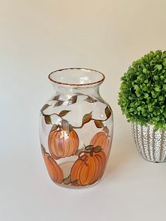 two vases sitting next to each other on a white surface with a green plant in the middle