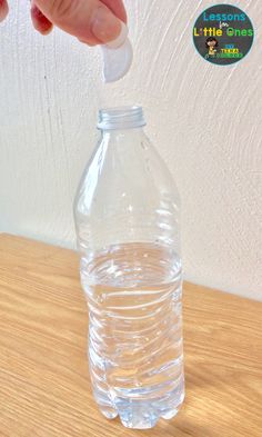 someone is pouring water into a plastic bottle on a wooden table with a white wall in the background