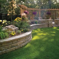 an outdoor garden with grass and flowers on the ground, surrounded by stone retaining walls