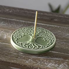 a green candle holder with a stick in it on a wooden table next to a potted plant