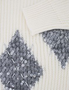 a white sweater with silver sequins and buttons on the side, next to a pair of scissors