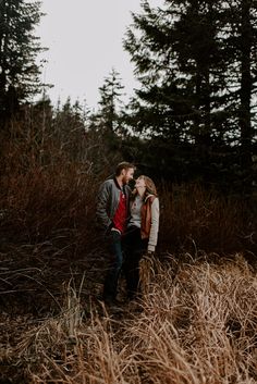 a man and woman standing in tall grass with trees in the backgrouds