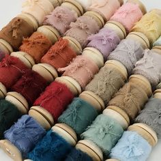 many different colors of thread on wooden spools with lace and bows in them