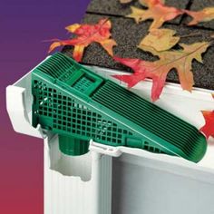 a green gutter guard on the side of a house with fall leaves around it