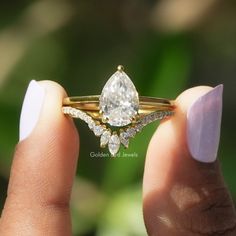 a woman's hand holding a gold ring with a pear shaped diamond