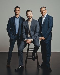 three men in suits are sitting on a stool and posing for the camera with one man wearing a suit