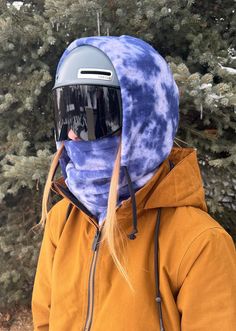 a person wearing a blue tie - dye ski mask and yellow jacket with trees in the background