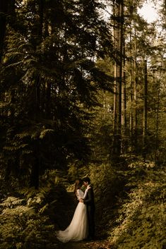 a bride and groom standing in the woods