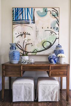 two blue and white vases sitting on top of a wooden table next to a painting