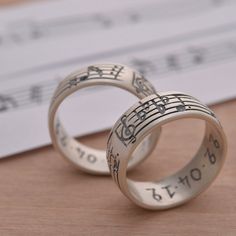 two wedding rings with musical notes engraved on them, sitting next to each other in front of a sheet of music