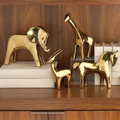 three gold giraffe figurines sitting on top of a wooden shelf