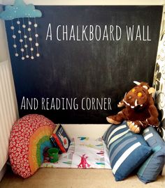 a stuffed animal sitting on top of pillows in front of a chalkboard wall and reading corner