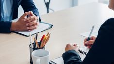 two people sitting at a table with notebooks and pens