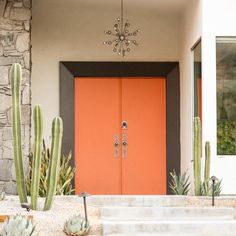 an orange door in front of a house with cacti and succulents