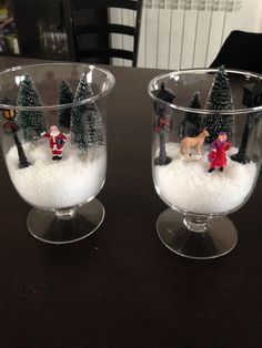 two small glass bowls with snow and christmas decorations in them on top of a table