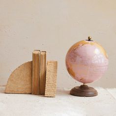 a pink globe sitting on top of a wooden block next to an open book and a piece of wood