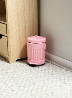 a pink trash can sitting in front of a wooden cabinet next to a white carpet