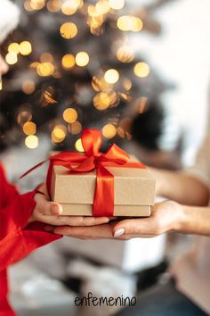 a person holding a present box with a christmas tree in the background