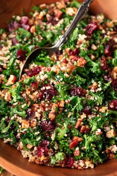 a wooden bowl filled with greens and cranberries next to a metal utensil