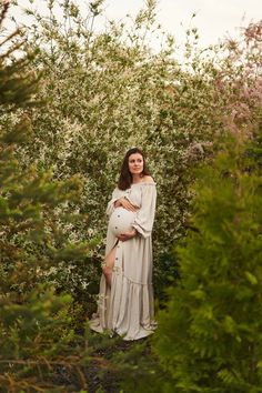 a pregnant woman standing in the middle of some bushes with her hands on her belly