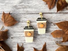 two small cup shaped earrings sitting on top of a wooden table next to autumn leaves