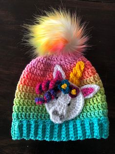 a crocheted hat with a unicorn on it and a multicolored pom - pom