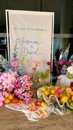 flowers and fruit are on display in front of a welcome sign for the wedding of jasmine and david