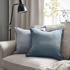 two blue pillows sitting on top of a couch next to a lamp