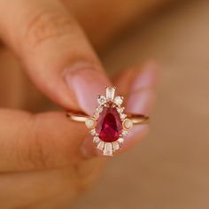 a woman's hand holding an engagement ring with a pear shaped ruby and white diamonds