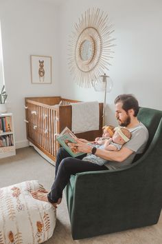 a man sitting in a chair holding a baby and reading a book to his child