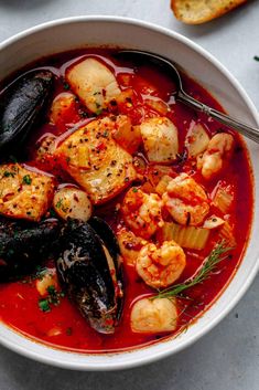 a white bowl filled with seafood and mussels on top of a table next to bread