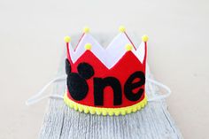 a small red and black crown with the word one on it's side sitting on top of a piece of wood