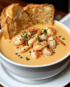 a bowl of soup with shrimp and bread on the side