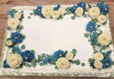 a square cake with white and blue flowers on the top is sitting on a wooden table