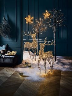 two deer statues with christmas lights on them in the middle of a wood floored room