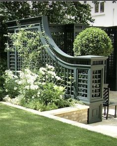 an outdoor garden with white flowers and green trelliss on the side of it