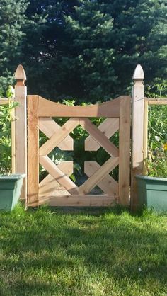 a wooden gate in the grass with potted plants on either side and trees behind it