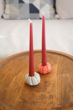 two red candles sitting on top of a wooden table next to a white candle holder