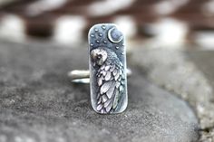 This listing is for one striking and unique sterling silver barn owl and moon ring. It features a detailed and dimensional barn owl under a crescent moon with stars. This thick and sturdy owl focal is fired onto 9 gauge half round wire. This ring is perfect for any owl and nature lover! It looks great solo or stacked with other rings and bands. - Choose your size at check-out! - Owl focal measures 28 mm by 12mm. - Ring band is 2mm wide by 1.5mm thick. - Made to order just for you! Please take note of estimated delivery times in the shipping section at checkout! Want to stack it with some awesome textured silver stacking bands? Find them here: https://www.etsy.com/listing/532906393/silver-stacking-rings-simple-silver-ring?ref=shop_home_active_16 Not sure of your ring size? Purchase one of t Barn Owl Ring, Spooky Jewelry, Witch Ring, Tattoo Jewelry, Geometric Owl, Witch Rings, Ring Moon, Owl Ring, Silver Rings Simple