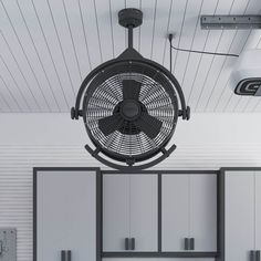 a black fan hanging from the ceiling in a room with white walls and cupboards