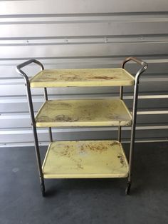 three tiered metal cart with wheels in front of a garage door and wall behind it