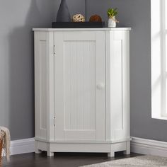 a white corner cabinet in a room with grey walls and rugs on the floor