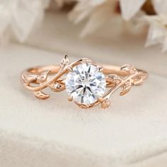 a rose gold engagement ring with a round diamond center surrounded by vines and leaves on a white background