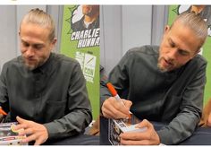 a man sitting at a table with two pens in his hands and another person writing