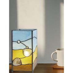 a stained glass vase sitting on top of a wooden table next to a coffee cup