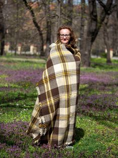 a woman wrapped up in a blanket standing on the ground with purple flowers around her