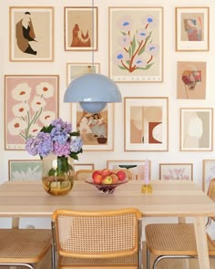 a dining room table with chairs and pictures on the wall above it, along with vases filled with flowers